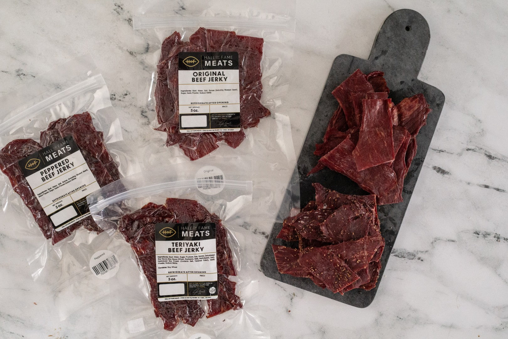 Meat jerky packages and a cutting board with jerky on a marble surface