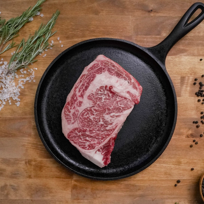 Raw Ribeye in a cast iron skillet on a wooden surface with herbs and spices.