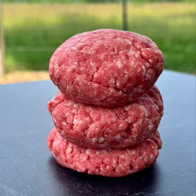 Three raw ground beef patties on a gray surface with a blurred green background